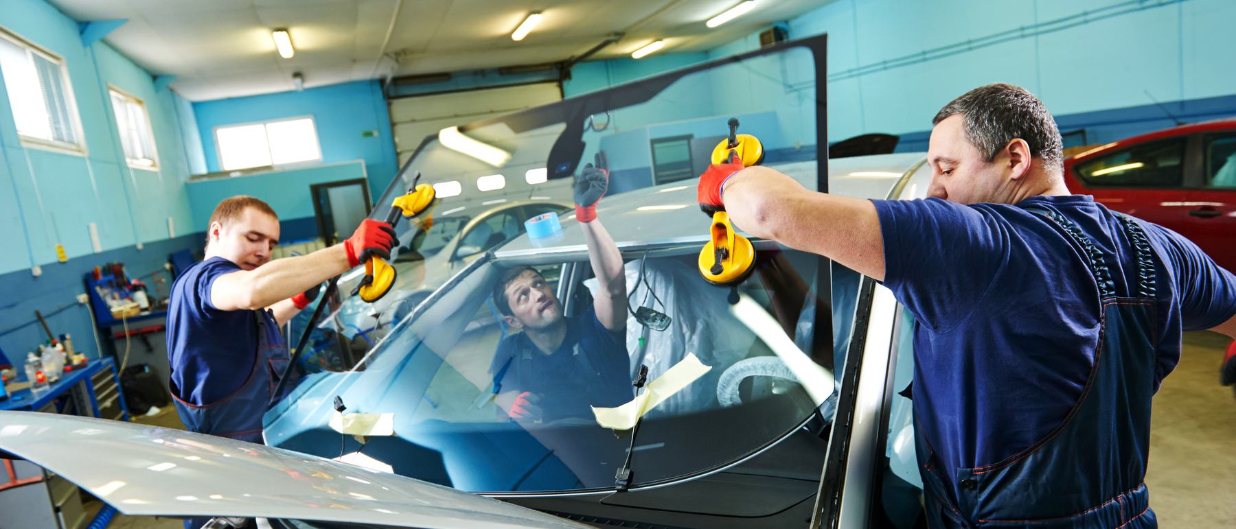 Zwei Autoglaser setzen in der Halle von Autoglas Blitz eine neue Windschutzscheibe ein